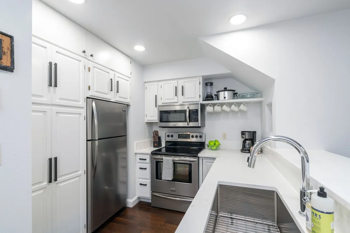 A modern, fully equipped kitchen with gleaming stainless steel appliances, pristine white cabinetry, and a spacious island for meal prep or casual gatherings. The kitchen area is bright and inviting, ideal for both cooking and entertaining.