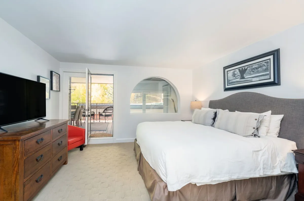 A serene master bedroom featuring a king-size bed, wooden dresser, and decorative artwork. The open door leads to a private balcony, allowing natural light to fill the space and offering an inviting spot for morning coffee or evening relaxation.