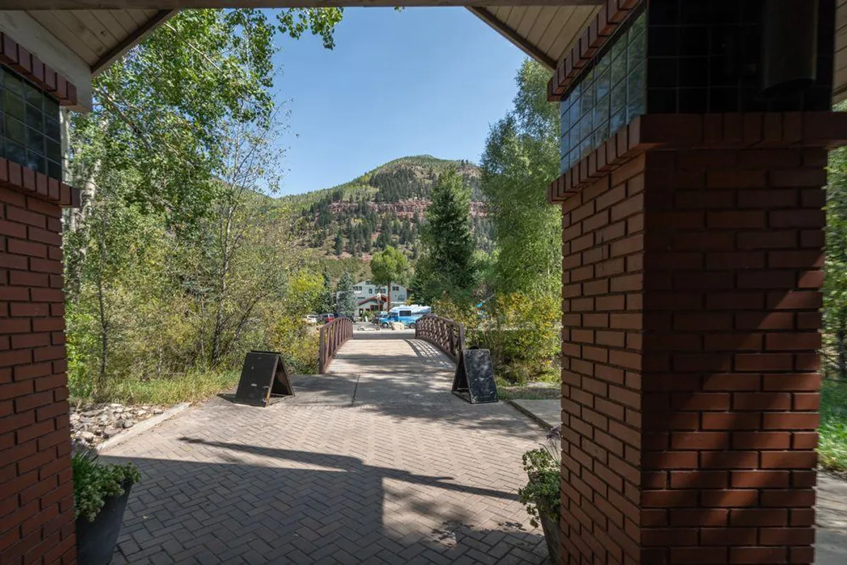 A welcoming arched entrance leads to a charming pathway surrounded by lush greenery and a picturesque bridge, creating a sense of invitation and connection to the outdoors.
