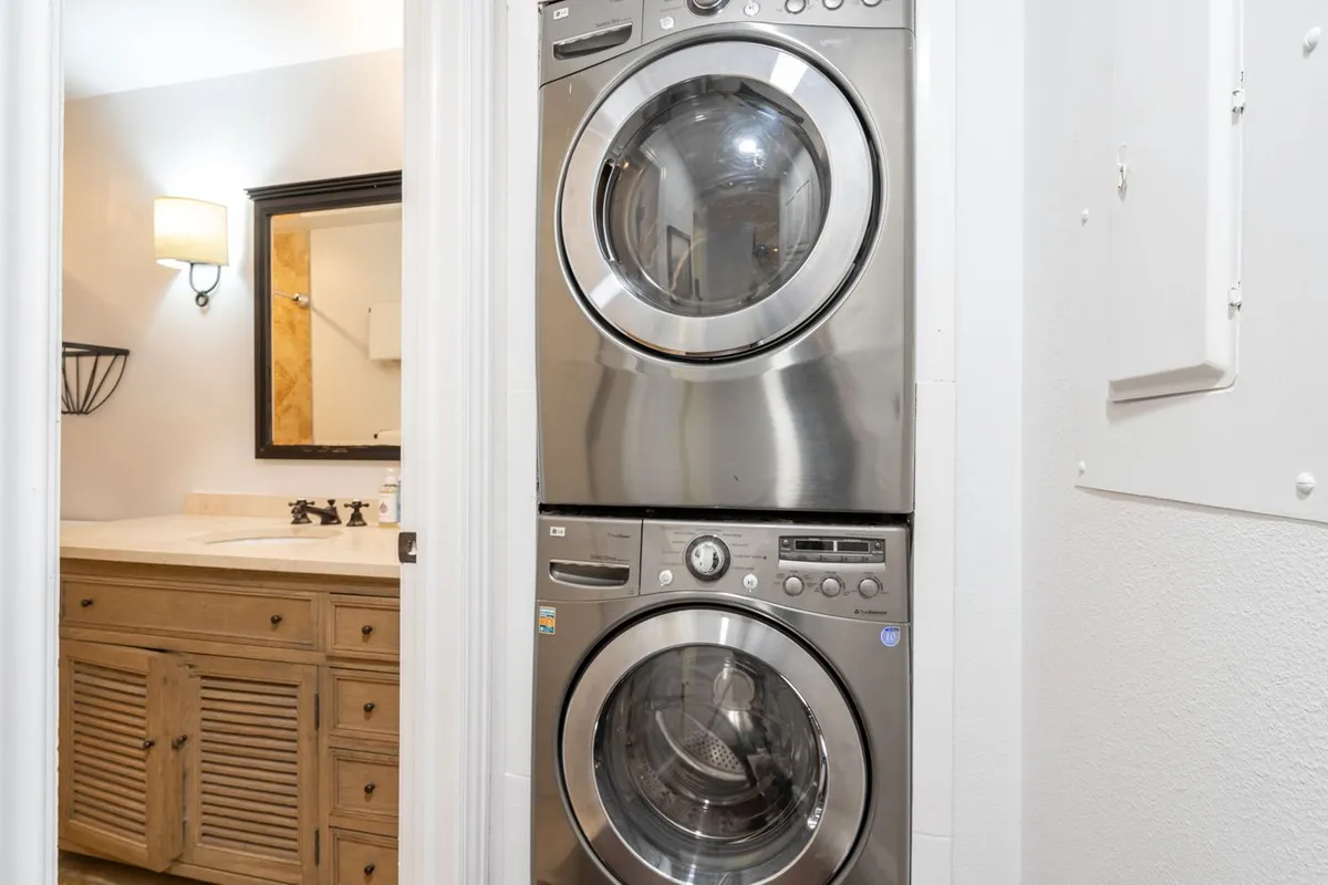 The photo displays a practical laundry area with a stacked washer and dryer, a vanity with a sink, and a mirror. The space is clean and organized, offering essential conveniences for longer stays or active vacations.