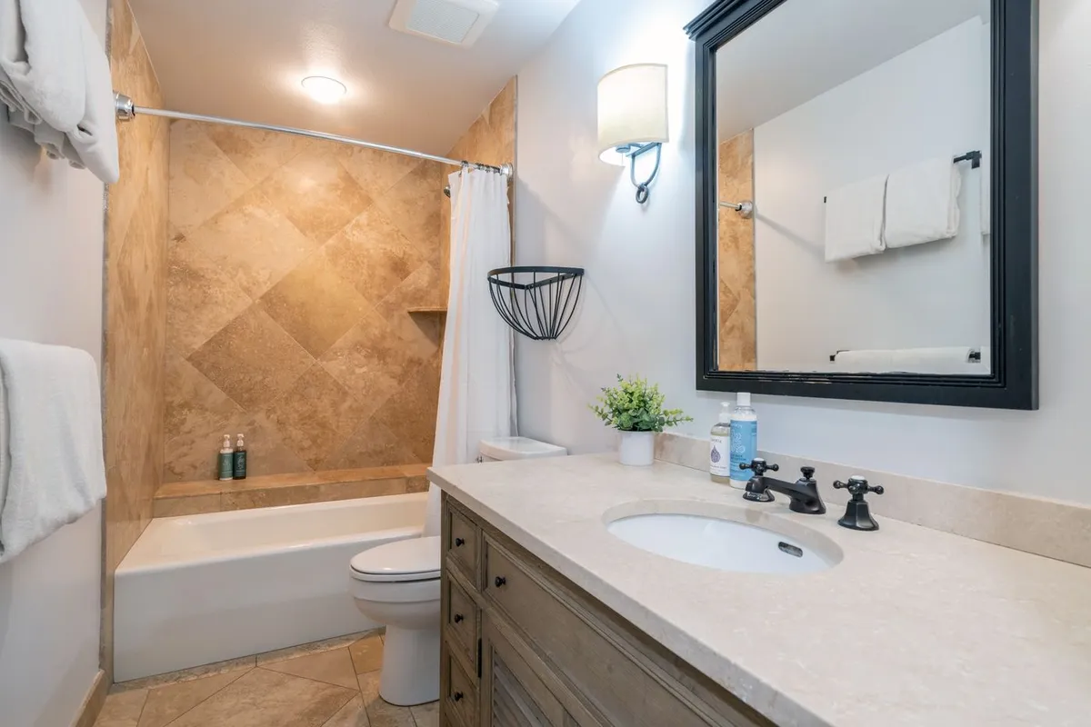 A well-appointed bathroom with a vanity, sink, framed mirror, bathtub, and tiled wall. The soothing atmosphere is perfect for relaxing baths or quick morning routines, serving both the master and guest rooms.