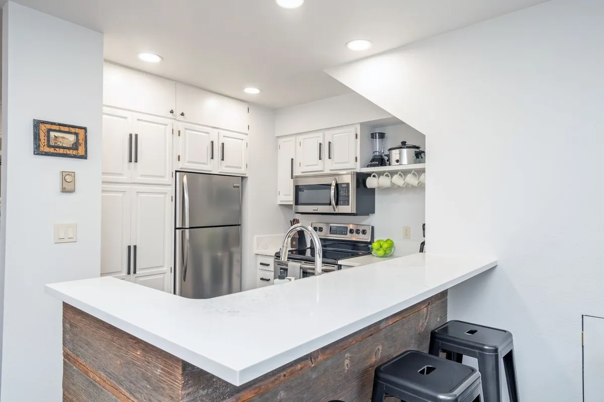 The image showcases a modern condo kitchen with a spacious island, sleek stainless steel appliances, and crisp white cabinetry. The layout invites conversation, with space for cooking, socializing, and gathering with family and friends.