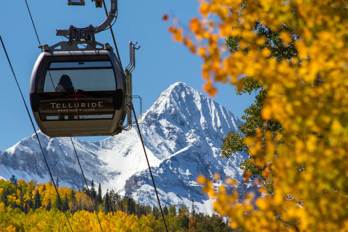A gondola glides above colorful autumn foliage and snow-capped mountains, merging the excitement of Telluride’s mountain adventures with easy accessibility from town.