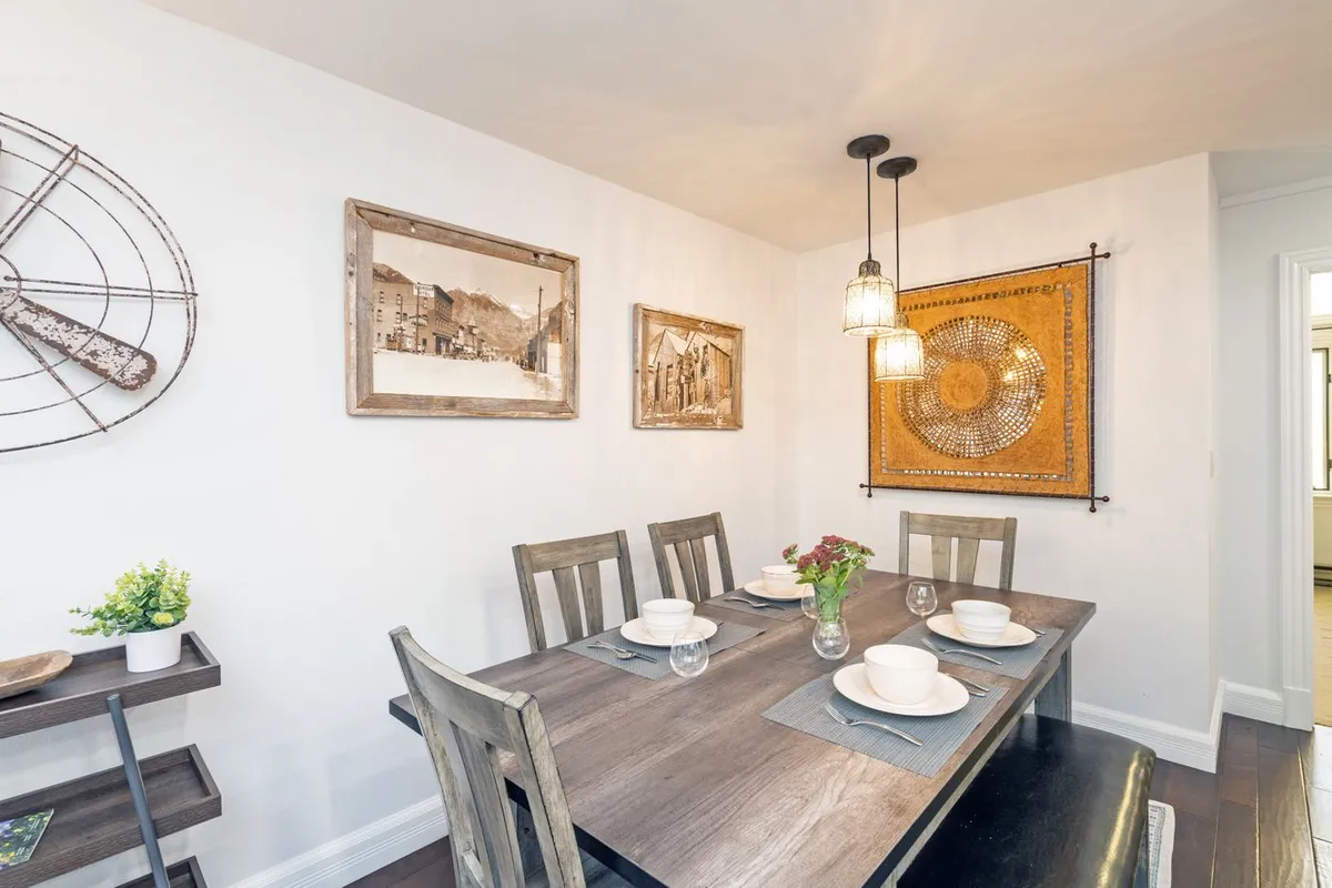 A warm and welcoming dining area with a sturdy dining table, artistic wall décor, ambient lighting fixtures, and a shelf with greenery. The scene is set for family meals, dinner parties, and casual gatherings, exuding a sense of comfort and togetherness.