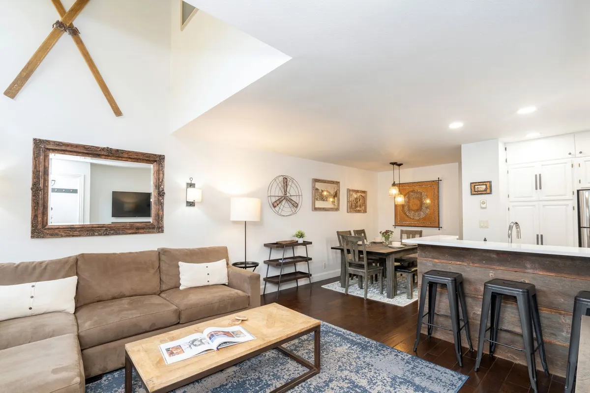 A cozy, open-concept great room featuring a comfortable sofa, a coffee table perfect for board games or drinks, a dining table ideal for shared meals, stylish bar stools at the kitchen counter, and tasteful wall decor. The space is unified and inviting, designed for relaxation and socializing.