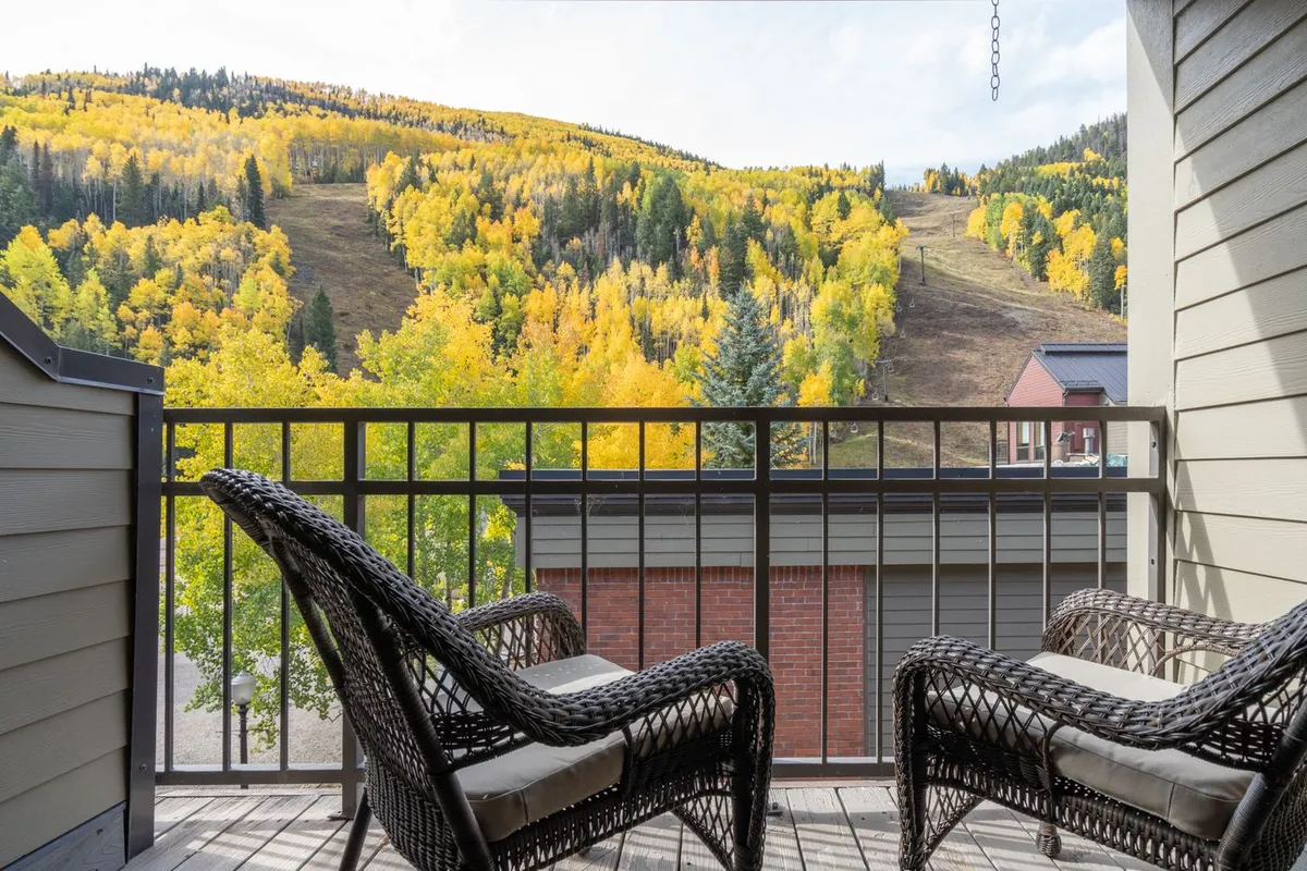 A private balcony with chairs overlooking colorful autumn trees and a mountain slope. The serene setting provides a scenic escape accessible from the master suite, perfect for unwinding or enjoying the fresh air.
